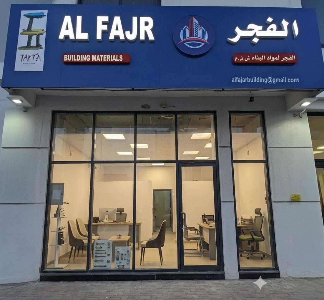 Al Fajr Building Materials storefront and office in Umm Al Quain, United Arab Emirates, with staffed desks visible through the glass frontage